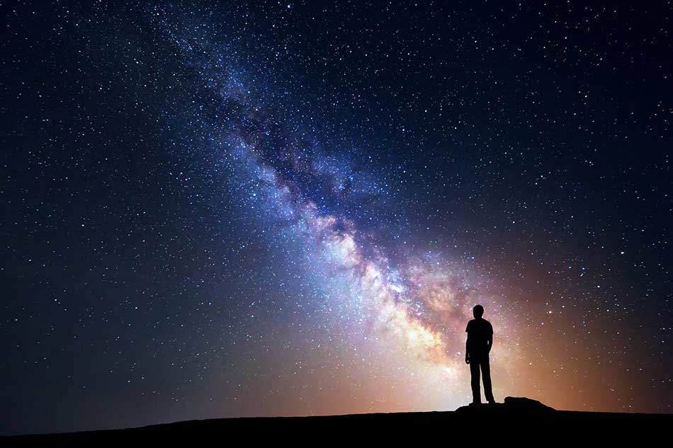 A silhouette of a person standing on a hill looking at the milky way